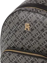 Mochila Tommy Hilfiger confeccionada en poliuretano con estampado integral de monograma TH. Presenta un compartimento principal con cierre, un bolsillo frontal con cremallera y herrajes metálicos dorados, incluyendo el logo de la marca en el frente. Cuenta con correas de hombro ajustables y un asa superior.