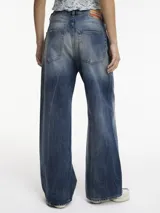 Pantalón de jean de tiro medio con pierna ancha, color azul con efecto desgastado y roturas en la parte delantera.