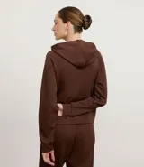 Campera deportiva color marrón, con capucha ajustable mediante cordón con lettering estampado, cierre frontal por cremallera, mangas largas con puños ajustados, bolsillo canguro y recorte en la espalda.