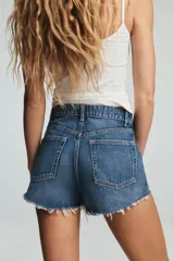 Short de jean de tiro alto, color celeste claro desgastado, con roturas grandes y deshilachado en el bajo. Presenta cinco bolsillos y cierre frontal con botón metálico.