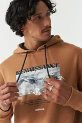 Canguro color tostado con capucha y cordones azul marino, con estampa frontal de la obra 'La creación de Adán' de Miguel Ángel, la palabra 'Renaissance' en mayúsculas y el logo de la marca Mistral.