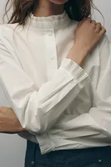 Camisa blanca de algodón con cuello con volantes y mangas largas con puños fruncidos.