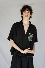 Remera oversize negra de piqué de algodón con bolsillo estampado con una palmera Phoenix Canariensis. Tiene elástico verde con hebilla de ajuste en la parte inferior.