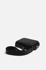Bandolera negra de nylon con solapa y cierre magnético. Tiene correa ajustable con mosquetón y bolsillo interior.