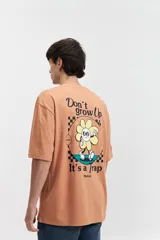 Remera de manga corta color salmón, de corte holgado con estampado en la espalda que incluye una flor con cara y texto.