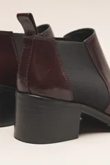 Botín negro de cuero vacuno con acabado charol, estilo botín Chelsea con puntera fina y elástico lateral. Posee un taco ancho y bajo de 5.5 cm.