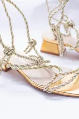 Sandalias doradas con tiras de cuerda para atar al tobillo.