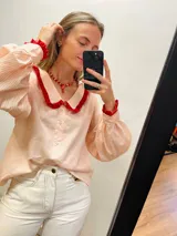 Camisa de algodón a rayas verticales color rosa y blanco, con cuello babero y puños con volantes rojos.
