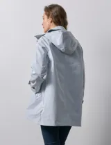 Gabardina color beige, impermeable, con abertura central con botones, bolsillos delanteros y capucha desmontable.