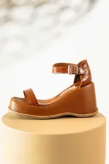 Sandalias de cuero color marrón con plataforma y taco de cuña. Tiras anchas con textura tipo cocodrilo y hebilla metálica plateada.