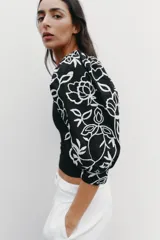 Top negro de escote pico con detalle de fornitura y mangas 3/4 abullonadas con estampado de flores bordadas.