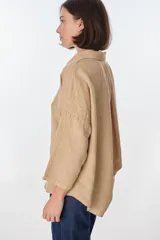 Camisa de lino color blanco, de manga larga y corte holgado, con cuello camisero y cierre frontal de botones.