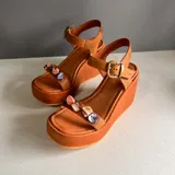 Sandalias de cuero color camel con plataforma y taco de cuña. Tira delantera decorada con piedras de nácar y tira al tobillo con hebilla dorada.