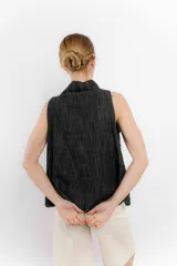 Chaleco de jean sin mangas con cuello en V y cierre frontal con botones metálicos. Tiene dos bolsillos de parche en el pecho y corte recto.