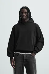 Sudadera con capucha color crudo, de corte relajado, confeccionada en tejido de algodón con interior rizado. Cuenta con cuello con capucha, manga larga, bolsillo frontal tipo canguro y acabados en rib.