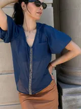 Camisa de gasa color gris oscuro, con mangas globo y una tira central vertical decorada con piedras azules.