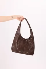 Bolso hobo marrón de símil cuero con bolsillo frontal y tachas plateadas en el contorno.