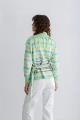 Saco de lana con diseño de rayas horizontales en tonos beige, marrón y negro. Presenta cuello en V con detalle de flecos y lazos laterales para ajustar.