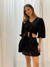 Minifalda negra con bordado inglés, cintura alta y detalle de argollas metálicas en el lateral.