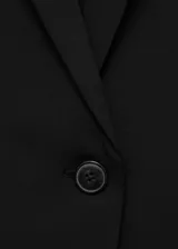 Blazer negro de diseño entallado, con solapas de muesca, hombros estructurados y cierre frontal de un solo botón. Presenta dos bolsillos de ribete delanteros y un bolsillo de ribete en el pecho.