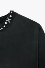 Remera negra de algodón con efecto lavado y cuello redondo con apliques de joyas plateadas.