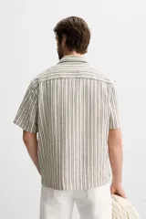 Camisa de hombre relaxed fit confeccionada en tejido de algodón a rayas verticales blancas y negras. Tiene cuello bowling, manga corta, bajo con aberturas laterales y cierre frontal de botonadura.