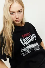 Remera negra de algodón con estampado frontal de un Chevrolet Camaro clásico y la inscripción "Chevrolet Camaro" en blanco y rojo.