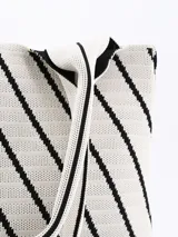 Bolso tipo tote de tejido de punto color crudo con diseño de líneas diagonales negras formando figuras geométricas. Tiene doble asa corta de hombro.