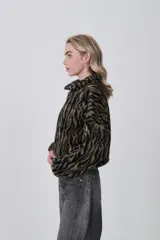 Campera corta de tejido peluche (corderito) con cierre frontal y cuello camisero. Presenta un estampado animal print de cebra o tigre en tonos marrón claro y negro.