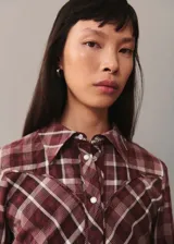 Camisa de manga larga con estampado de cuadros en tonos borgoña, blanco y gris. Tiene cuello camisero, cierre frontal con botones a presión y corte recto.