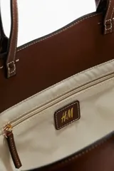 Bolso shopper de lona color beige con detalles en cuero marrón. Tiene doble asa de mano y compartimento interno con cierre.