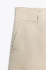 Bermuda color beige de lyocell, con tiro alto, trabillas en la cintura, bolsillos laterales con solapa, bolsillos de vivo en la espalda y cierre frontal con cremallera, botón y gancho metálico.