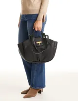 Cartera tote negra de ecocuero con base redondeada y pliegues decorativos. Cuenta con una solapa central con herraje dorado en forma de "T" y asas dobles para hombro y mano. El interior tiene triple compartimento.