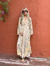 Vestido largo de seda con escote en V y mangas amplias, presentando un estampado paisley en tonos beige, rosa pálido y toques de amarillo.