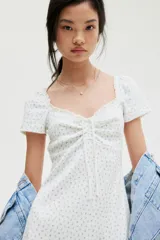 Vestido corto blanco con estampado floral celeste, de punto acanalado con escote corazón ribeteado en encaje y cordón para ajustar en el centro del busto. Modelo de manga corta con cuerpo entallado, copas preformadas y pollera con vuelo.