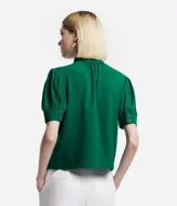 Blusa verde esmeralda de crepé con cuello alto, botones dobles y pequeña abertura en el cuello. Tiene mangas cortas abullonadas con botones.