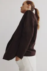 Blazer marrón oscuro con solapas de muesca, dos botones frontales y dos bolsillos de parche grandes en la parte inferior. Presenta canesú delantero y trasero y hombreras.