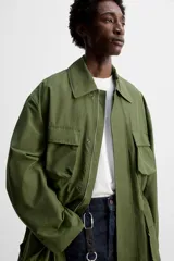 Parka verde militar de tejido técnico ligero, corte relaxed fit, cuello solapa y manga larga. Tiene cuatro bolsillos de plastrón con solapa en el delantero, cintura ajustable en el interior y cierre frontal con cremallera oculta por solapa con botones a presión.