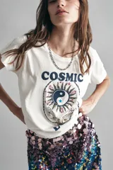 Remera blanca de algodón con cuello redondo y mangas cortas. Estampado frontal con la palabra "COSMIC" en azul y un diseño esotérico con detalles en flock, bordado con mostacillas e hilo de lurex.