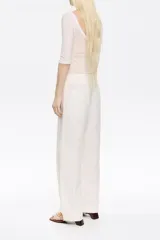 Pantalón blanco de lino y algodón, corte barrel, largo tobillero, con cierre frontal oculto, bolsillos delanteros y traseros, y cinturón de tela a tono.