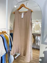 Vestido corto sin mangas, color beige claro, con cuello redondo y un volante o ruedo con volado en el bajo.