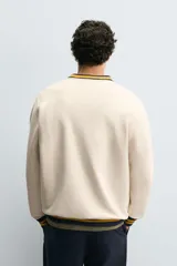 Sudadera color crema de corte regular fit, cuello redondo y manga larga. Presenta ribete a rayas en cuello, puños y bajo. Tiene un pequeño bordado de una flor en el pecho.