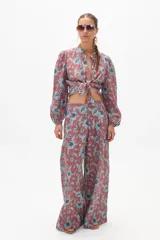 Conjunto de pantalón y blusa de lino con estampado floral en tonos terracota y azul. La blusa es de manga larga con cuello mao y se ata en la parte delantera. El pantalón es culotte de tiro alto con bolsillos laterales y cierre frontal escondido.