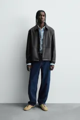 Cazadora de efecto piel color marrón oscuro, corte relajado, con cuello solapa, cierre frontal de botones a presión y bolsillos de vivo en cadera.