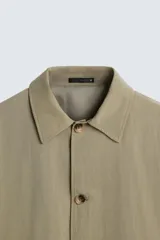 Gabardina color arena de corte amplio, con cuello solapa, manga larga, cierre frontal con botones y bolsillos laterales con solapa.