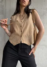 Chaleco color tostado de lino liviano con bordado de palmeras en la terminación y corte recto. Cierre frontal con botones.