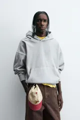 Sudadera gris con capucha ajustable, corte boxy fit, manga larga, bolsillo tipo canguro y estampado en la espalda.