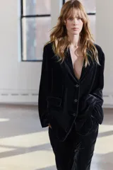 Blazer de terciopelo negro con cuello solapa de muescas, manga larga con abertura y botones, bolsillos con solapa y forro interior.