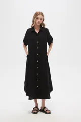 Vestido camisero midi negro de corte holgado, con cuello camisero, mangas cortas con trabillas, cierre frontal con botones, bolsillo en el pecho y bolsillos laterales.