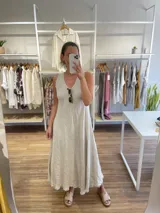 Vestido largo sin mangas, color beige claro, con escote en V y ruedo deshilachado.